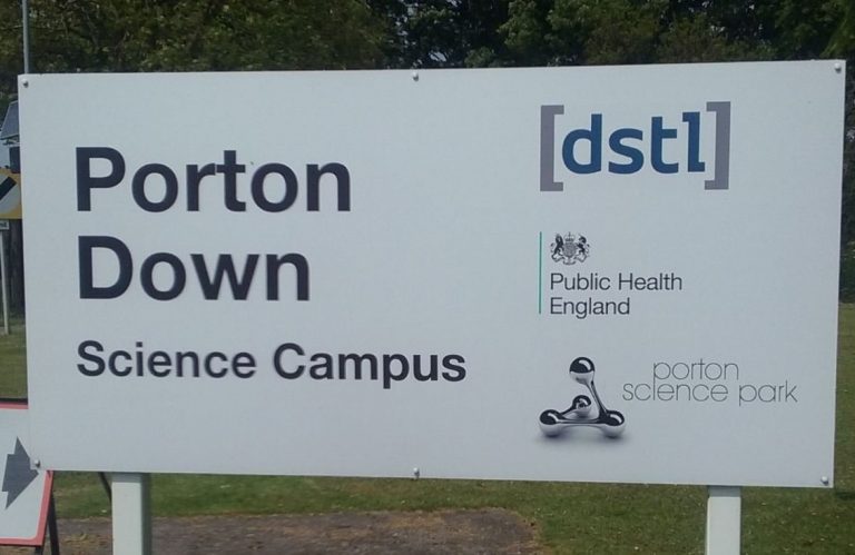 Sign for Porton Down Science Campus, displaying logos for DSTL, Public Health England, and Porton Science Park. As a pathfinder in innovative research, it plays a crucial role in the resettlement of scientific advancements from theoretic exploration to real-world applications.