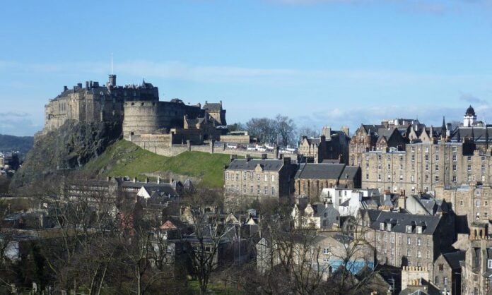 View of Edinburgh Castle perched on a rocky hill, surrounded by historic buildings under a clear blue sky, once serving as a strategic military stronghold.