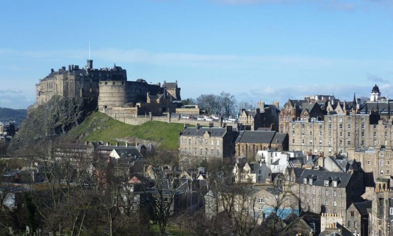 View of Edinburgh Castle perched on a rocky hill, surrounded by historic buildings under a clear blue sky, once serving as a strategic military stronghold.