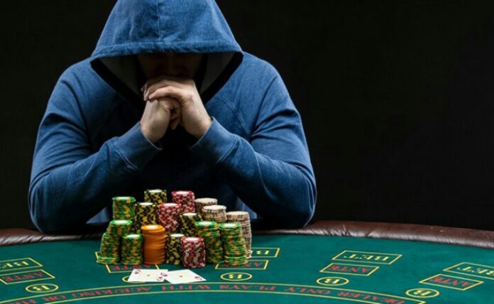 A poker table holds a veteran in a hoodie, surrounded by a large stack of poker chips and playing cards.