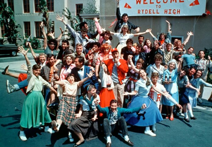 A large group of people in retro clothing pose joyfully in front of a building with a 