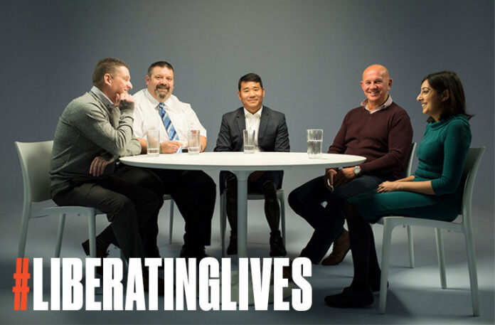 Five people, including a veteran, are sitting around a white table, smiling. The text 