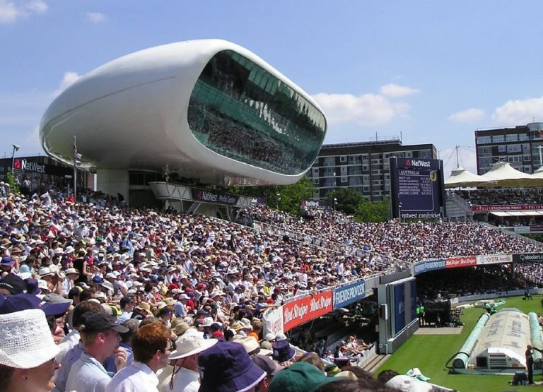 The crowd seated at a cricket stadium buzzed with excitement, the modern media center standing tall in the background like a fortress. Amidst the cheers, murmurs of past army tales and stories of resettlement floated through the air, adding layers to the vibrant atmosphere.