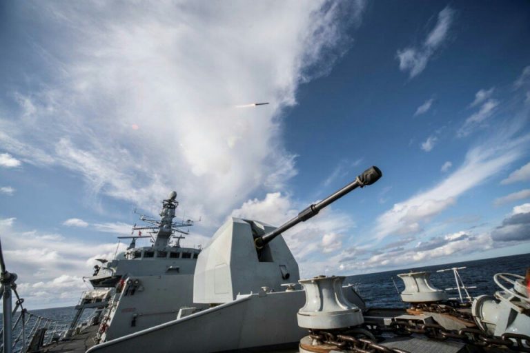 A naval pathfinder ship on open water features a visible cannon in the foreground, while a missile launches into the sky in the background, showcasing military prowess.