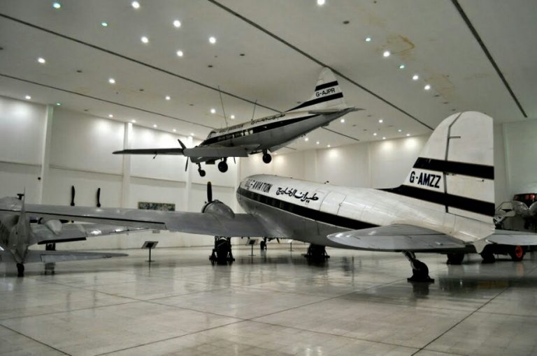 Two vintage aircraft, reminiscent of their Royal Navy service days, are displayed in a spacious, well-lit hangar. One aircraft is suspended in the air, while the other is grounded. Both proudly showcase their distinctive black and white military markings.