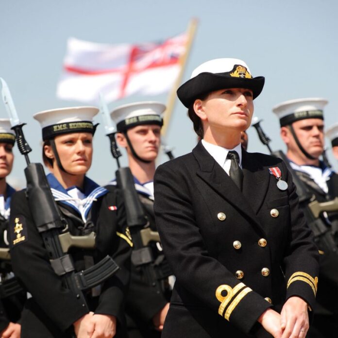 A naval officer in uniform stands before a group of sailors holding rifles, embodying military precision, with a naval flag waving proudly in the background.