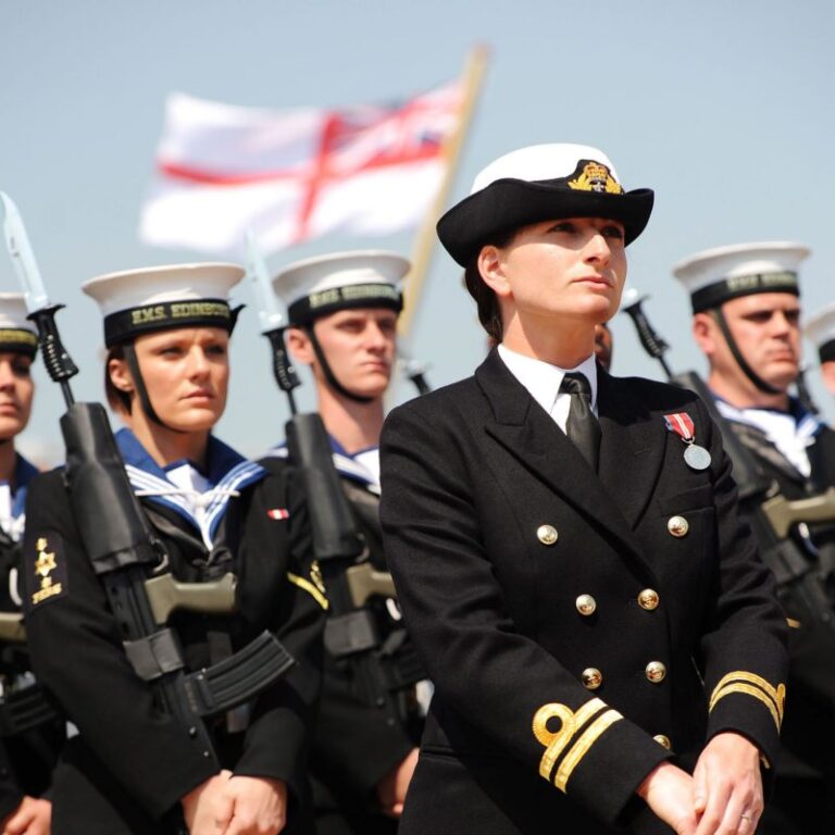 A naval officer in uniform stands before a group of sailors holding rifles, embodying military precision, with a naval flag waving proudly in the background.