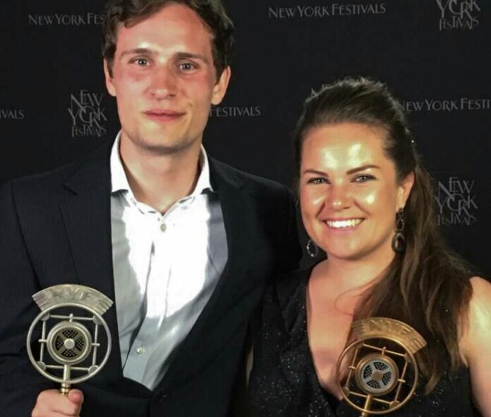 Two people smiling and holding awards against the 