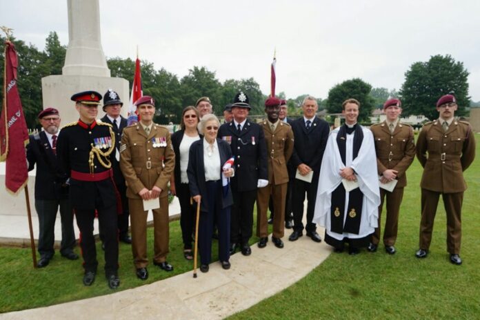 A group of people, including Army personnel and civilians, stand together on grass in front of a monument. Some wear uniforms and others are in formal attire, honoring the pathfinders and veterans among them.