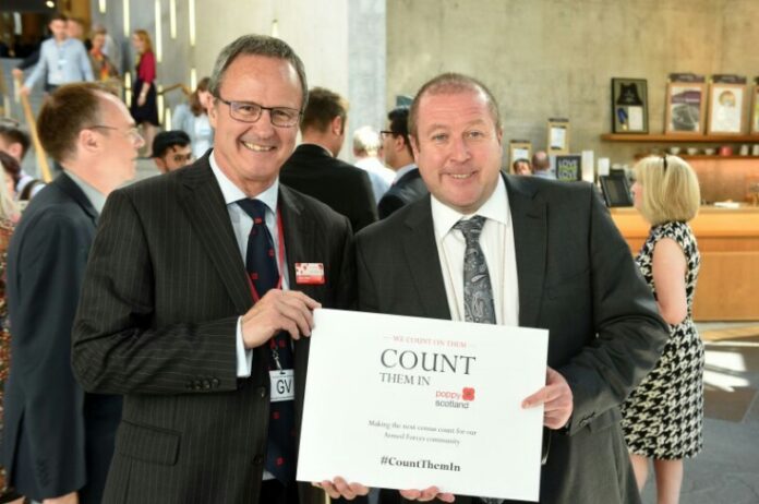 Two men in suits hold a sign promoting Poppy Scotland's 