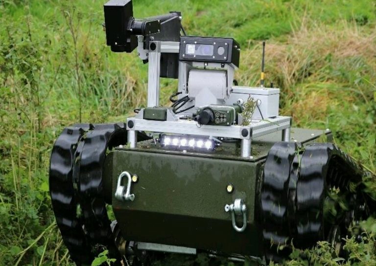 A green robot with tracks navigates through grassy terrain, equipped with cameras and sensors, its design inspired by military innovation, as it maneuvers deftly among the dense vegetation.
