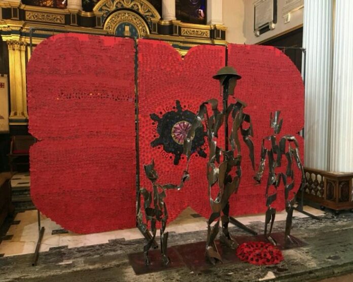 Metal statues of soldiers stand in front of a large poppy display inside a building, symbolizing the Army's commitment to remembrance and honoring those who have paved the path for resettlement and peace.