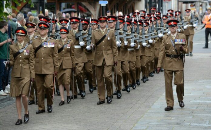 A group of uniformed soldiers, reminiscent of a disciplined Royal Navy unit, marches in formation down the street, led by a commanding officer.