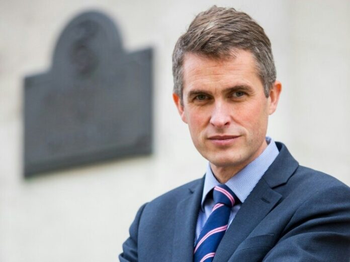 A man in a suit and tie stands with arms crossed, embodying the confidence of a pathfinder, in front of a blurred plaque on the wall.