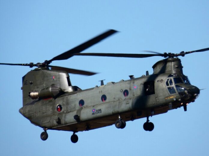 A military Chinook helicopter, a vital asset to the Army, soars gracefully against a clear blue sky, embodying the spirit of a pathfinder on its crucial mission.