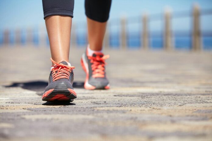 Close-up of a person walking along a paved path wearing gray and orange athletic shoes, reminiscent of the resilience found in military life, with a blurred background.