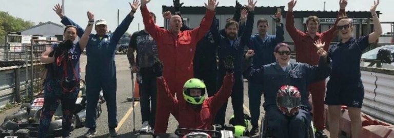 A group of people in racing suits and helmets, looking as thrilled as a military squad on a mission, pose excitedly next to go-karts on a track.