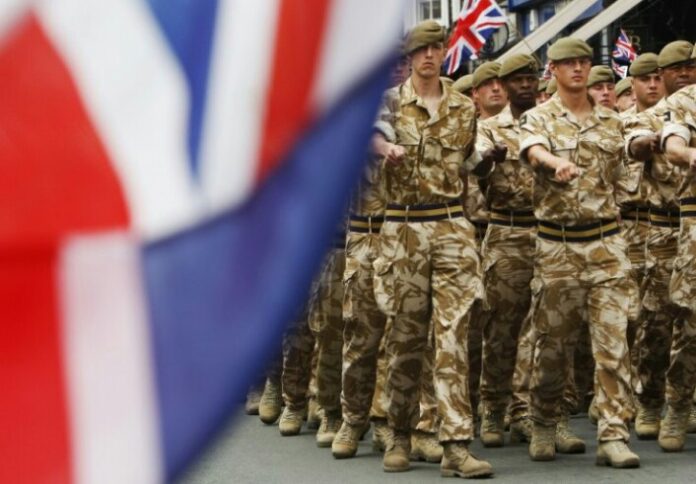 Soldiers in camouflage uniforms march in formation, their disciplined steps echoing pride as British flags wave prominently in the foreground and background—a powerful tribute to military tradition and steadfast service.