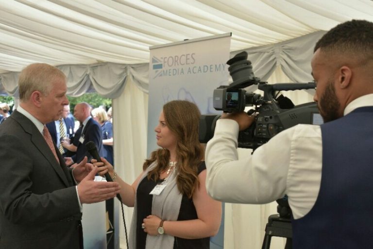 A reporter interviews a person at the event, with a camera operator capturing every moment. The "Forces Media Academy" banner stands prominently in the background, highlighting its connection to military pathfinder initiatives.