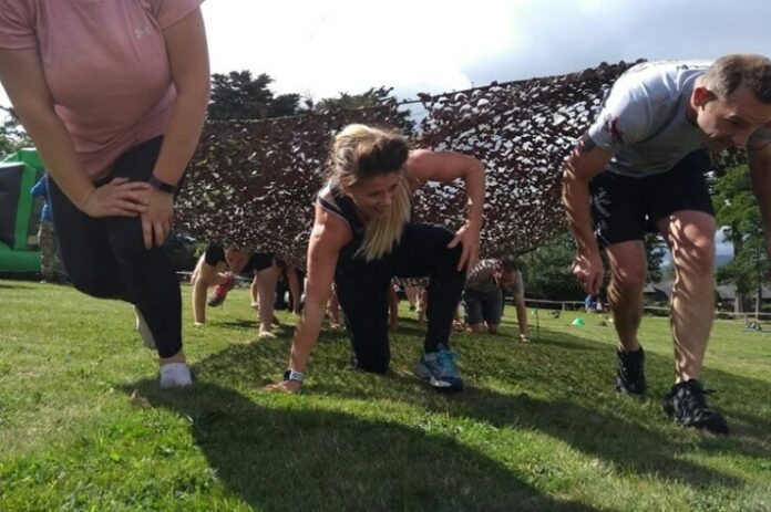 Participants are embracing the challenge of an outdoor obstacle course, crawling under a net on grass, just like seasoned veterans navigating their way through.