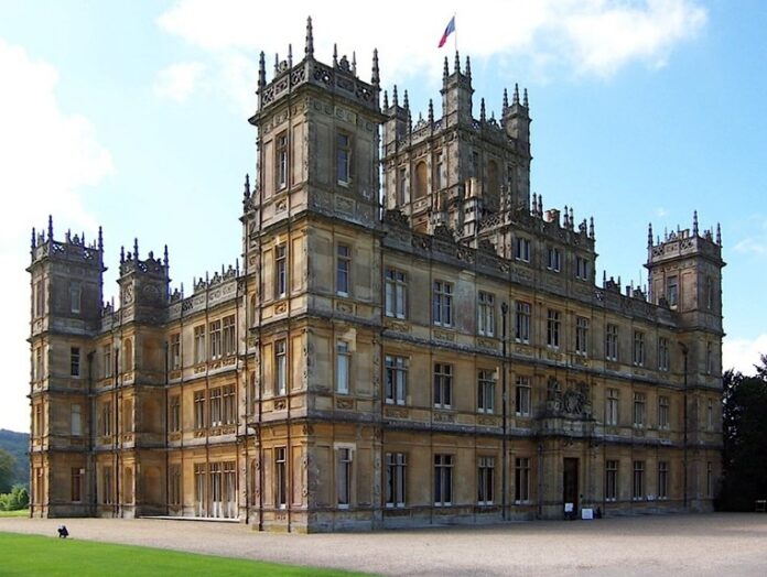 A large historic castle with tall towers and ornate architecture stands proudly, once a strategic military fortress. It is surrounded by a green lawn under a clear blue sky, echoing tales of army resettlement from its storied past.
