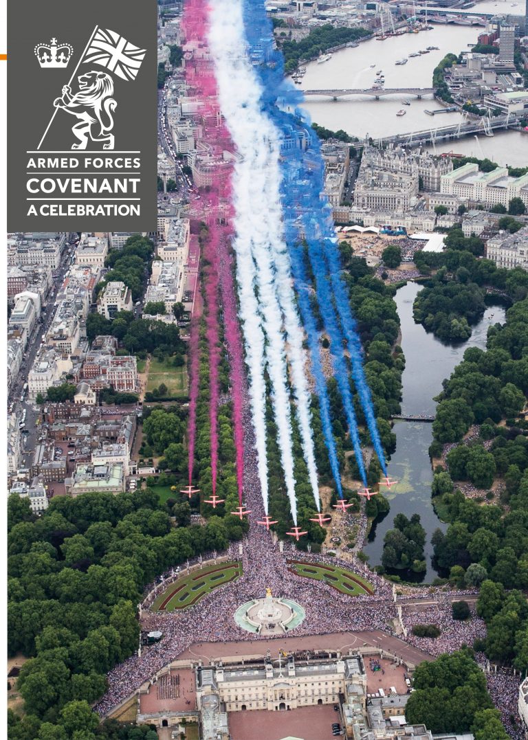 Aerial view of jets flying over a large crowd, leaving red, white, and blue trails in the sky near a park and river. The image features a banner for an Armed Forces celebration honoring veterans.