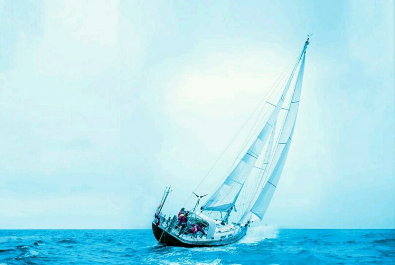 The veteran sailboat leans gracefully in the wind on the open sea, navigating its pathfinder journey under a cloudy sky.