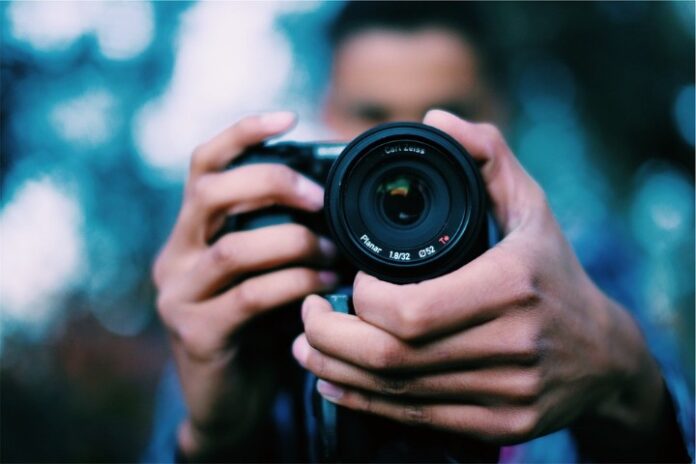 A person in a military uniform holds a camera, the lens facing forward with precision. The blurred background suggests a setting far from home, capturing moments that speak volumes about life in service.
