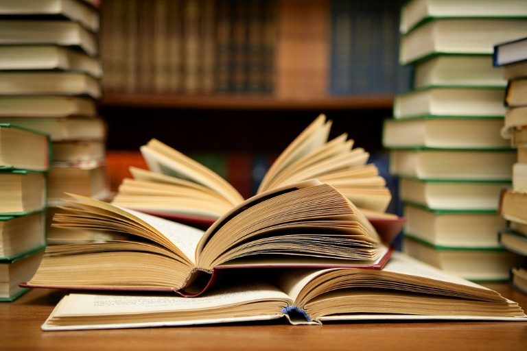 Open books are spread out on a table like a navigator's tools, with stacks of closed volumes reminiscent of a Royal Navy library in the background.