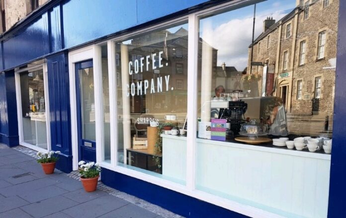 A street view of a coffee shop with large windows displaying coffee equipment and cups. 