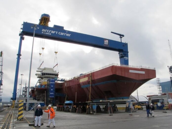 A massive ship under construction in the shipyard is supported by a crane labeled 
