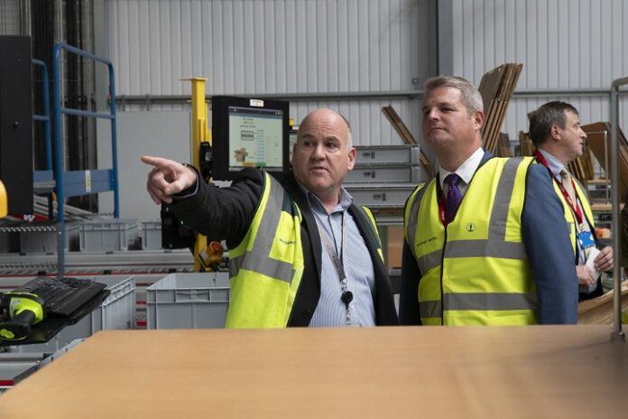 Two men in high-visibility vests stand in a warehouse, resembling seasoned Pathfinders navigating a complex space. One man is pointing and explaining something to the other, both focused intently on optimizing warehouse operations.
