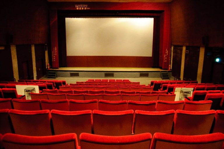 An empty cinema auditorium with red chairs resembles a silent salute to a veteran audience, their stories as vivid as the films projected on the large screen.