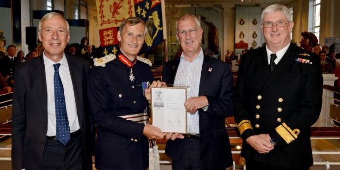 Four men in formal attire stand together indoors, with one proudly holding a framed document. Their poised demeanor suggests a connection to a prestigious program, perhaps related to Pathfinder or resettlement initiatives within the military community.