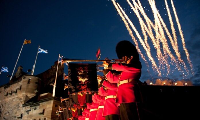 Royal guards in red uniforms play trumpets at the event, reminiscent of a grand military procession, with fireworks lighting up the night sky in the background.