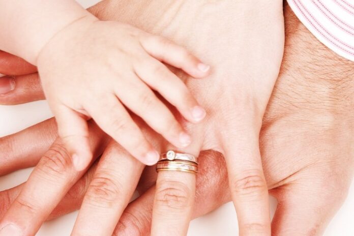A baby's hand rests on top of two adult hands with wedding rings, beautifully symbolizing family unity and the bonds often celebrated during National Adoption Week.