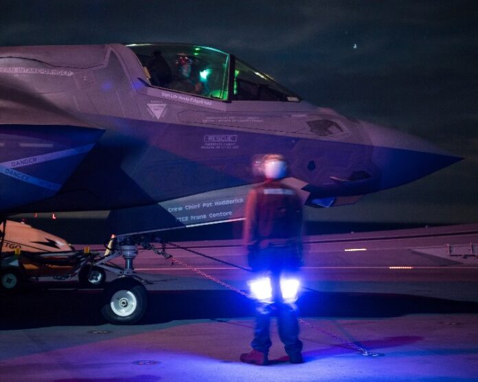 A veteran in a reflective vest guides a jet on a dimly lit runway, showcasing precision and dedication.