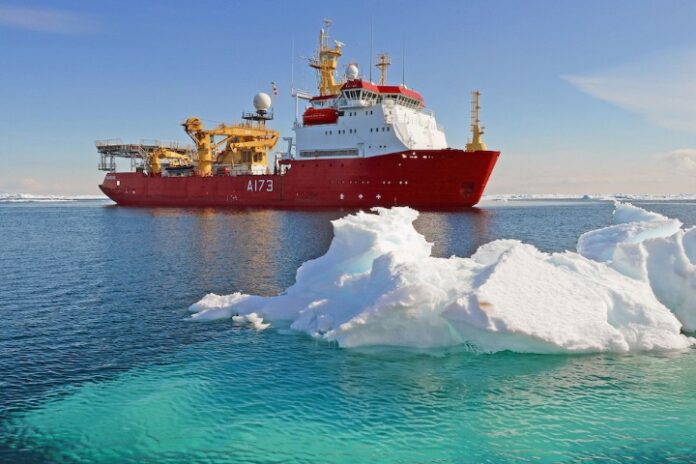 A red icebreaker ship, part of a significant Navy deal worth £1bn, navigates through calm Arctic waters, with partially submerged icebergs in the foreground.