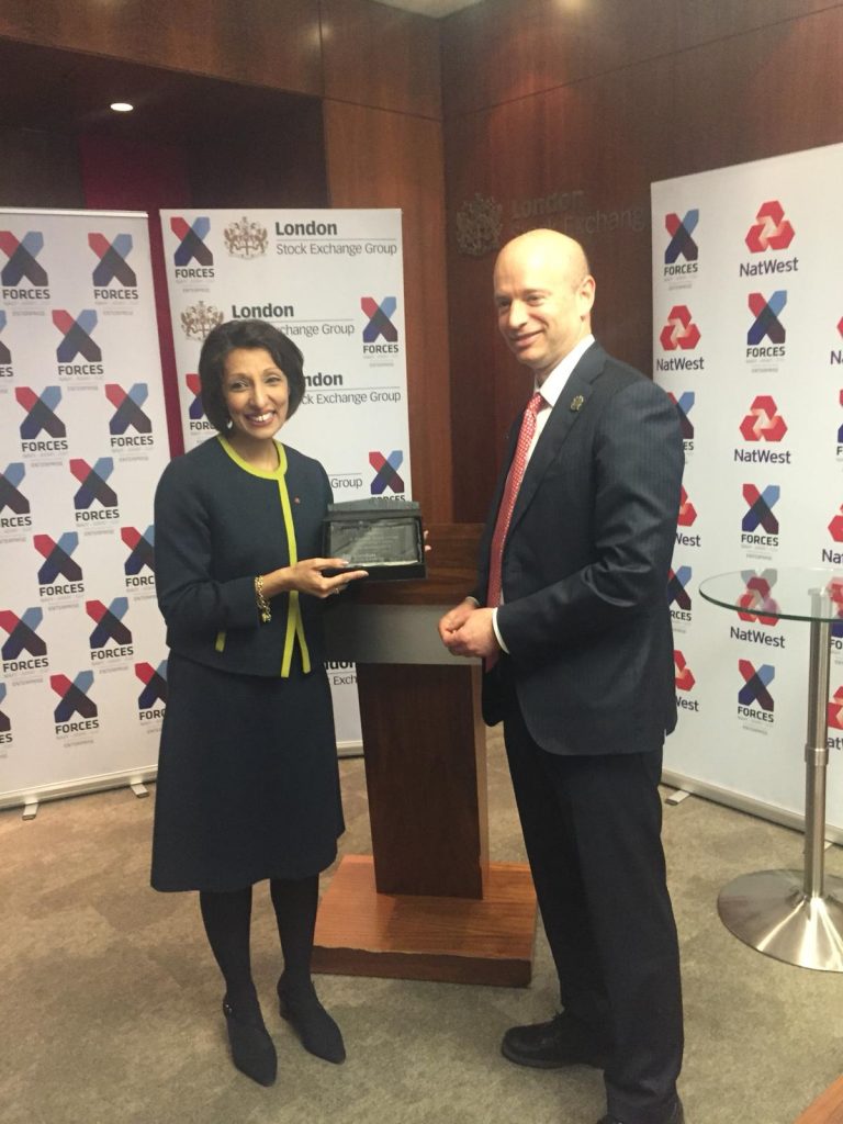 Two ex-military entrepreneurs stand by a podium, proudly holding a plaque. The background showcases banners with logos for London Stock Exchange Group, X-Forces, and NatWest, symbols of broader support for entrepreneurial ventures.