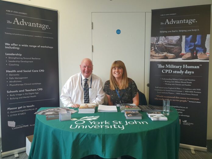At the York St John University event, where Nick Wood is featured, two people sit at a table surrounded by informative brochures promoting workshops and study days. Behind them, posters highlight the Resettlement Expo and its Pathfinder initiative.