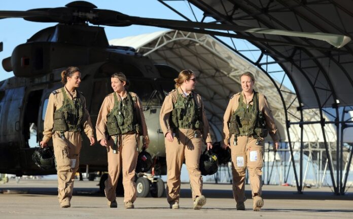 Four RAF Women of the Year, in sharp military uniforms, stride confidently in front of a helicopter sheltered under a hangar.