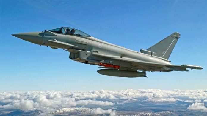 A fighter jet, watched closely by the Defence Secretary and his Qatari counterpart, flies above the clouds against a clear blue sky.