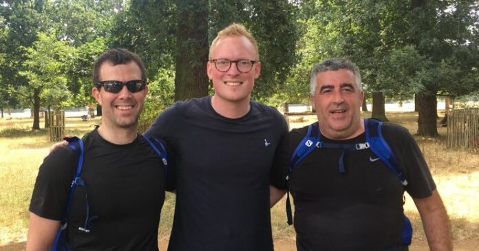 Three men in black athletic gear stand together outdoors, smiling against the backdrop of lush trees, reminiscent of the serene landscapes of Exmoor.