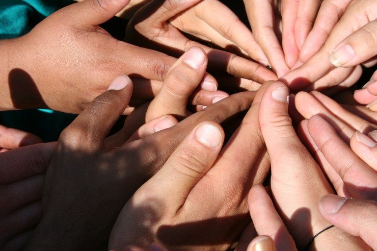 A group of diverse hands forms a circle, thumbs meeting at the center against a textured background, symbolizing support and solidarity for Forces Families.