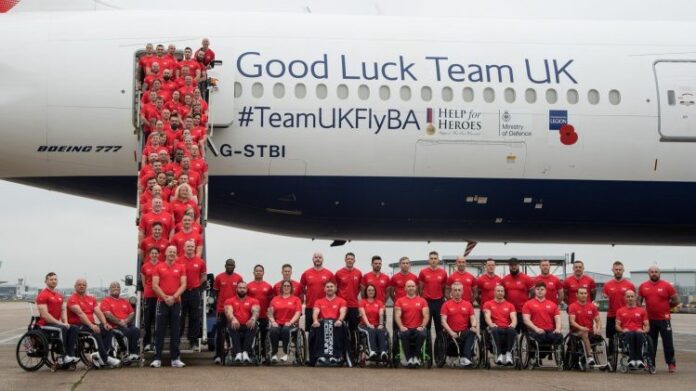 A group of people in red shirts, some in wheelchairs, pose in front of an airplane with 