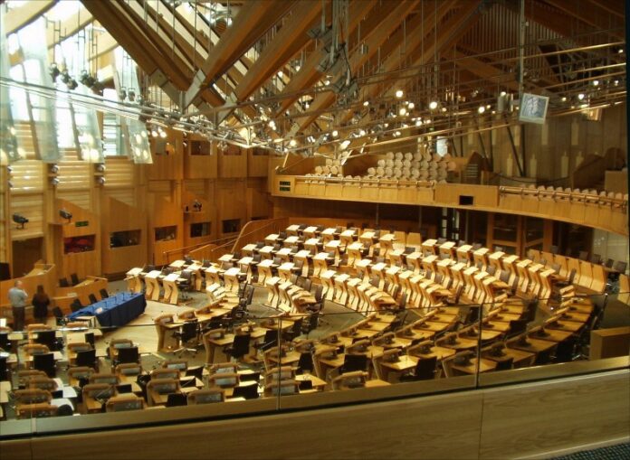The interior view of the modern, spacious parliamentary chamber boasts rows of desks and seating in a semi-circular layout under a high wooden ceiling, reflecting the dedication to public service akin to that supported by the Scottish Veterans Fund.