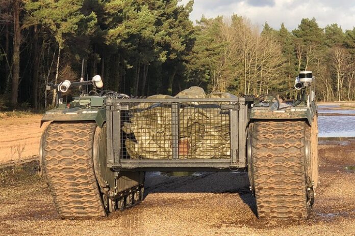 A rugged, remotely operated military vehicle with caterpillar tracks delivers supplies along a gravel path in a wooded area, part of an Army robot exercise.