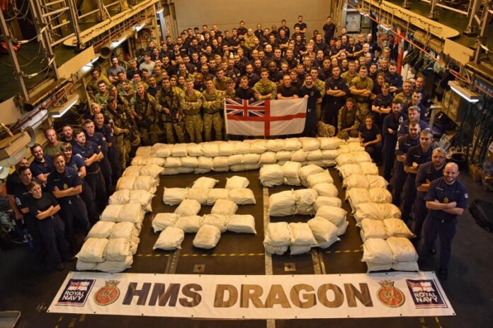 A group of navy personnel on the HMS Dragon ship pose around bags arranged to form 