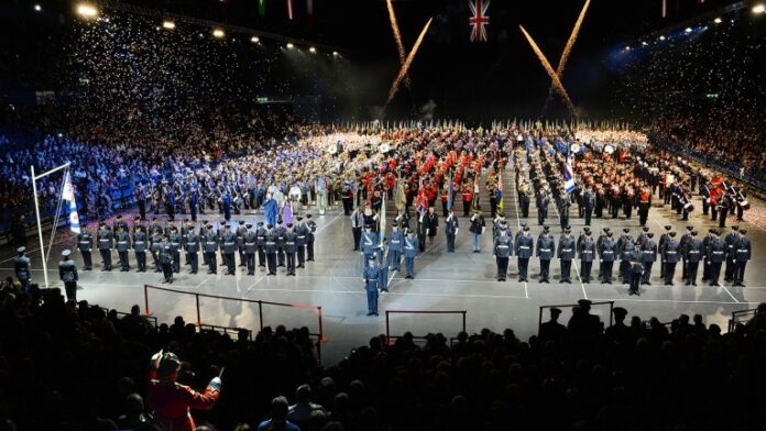 A large indoor ceremony, the Birmingham Tattoo features marching bands, military personnel, and flag bearers. Confetti falls from above as a crowd watches from the stands, paying tribute to those who once served at the Veterans' Care Home.