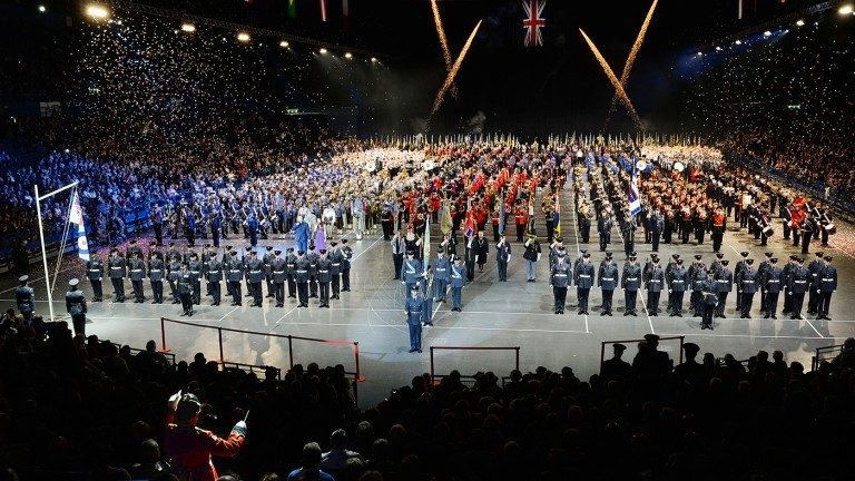 A large indoor ceremony, the Birmingham Tattoo features marching bands, military personnel, and flag bearers. Confetti falls from above as a crowd watches from the stands, paying tribute to those who once served at the Veterans' Care Home.